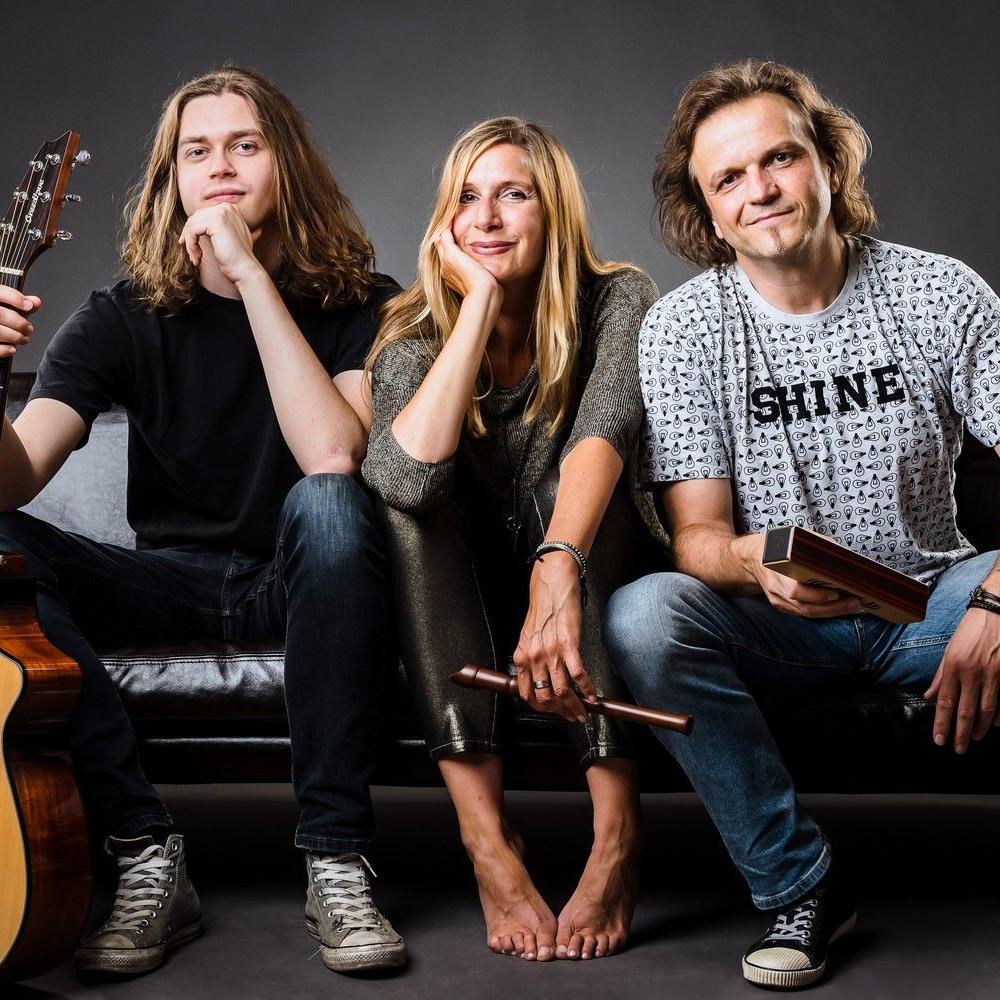 Die Band sitzt auf einer Ledercouch, links Anton mit seiner Gitarre, in der Mitte Stephanie auf ihre Hand gestützt und rechts Dirk mit einem Shaker in der Hand