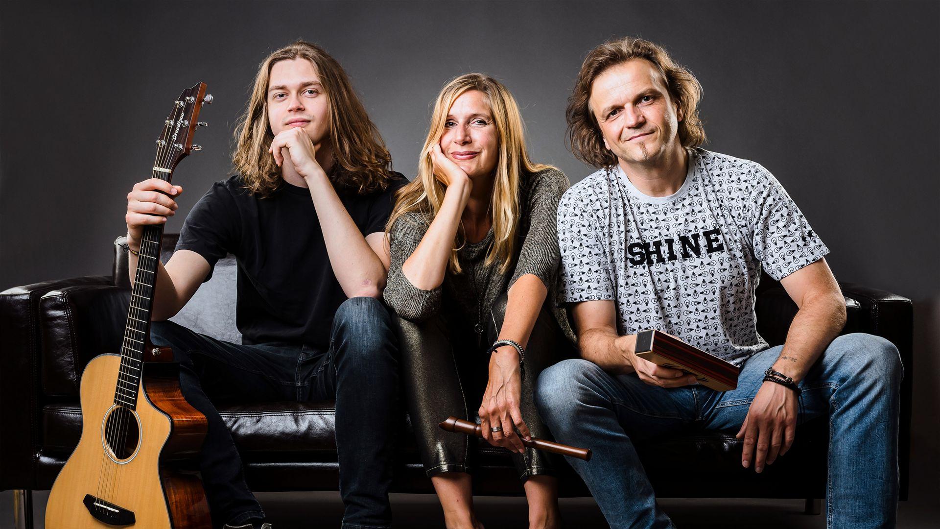 Gitarrist Anton, Sängerin Stephanie, Percussionist Dirk sitzen nebeneinander auf einer Couch und blicken freundlich in die Kamera